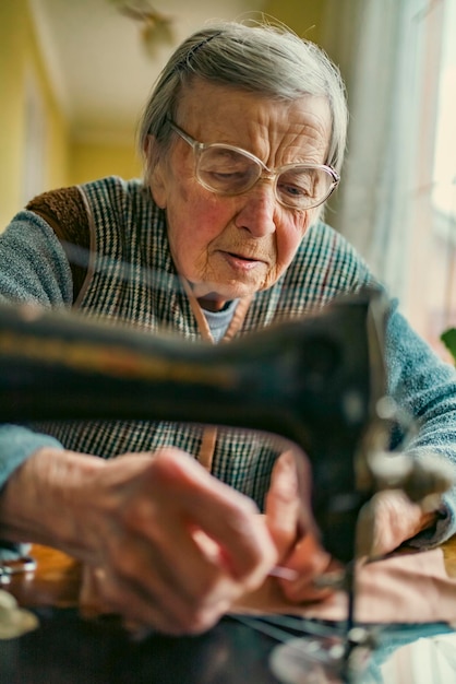 Ältere Frau mit Brille verwendet Nähmaschine faltige Hände der alten Näherinälteren Frau Alte Nähmaschine Klassische manuelle Nähmaschine im Retro-Stil, die für Näharbeiten bereit ist