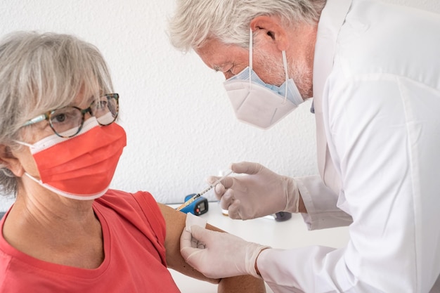 Ältere Frau mit chirurgischer Maske, die vom Arzt eine Auffrischimpfung gegen Covid19 erhält