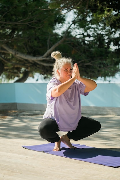 Ältere Frau mit Dreadlocks in Dehnungsposition am Meer am Morgen Ältere Frau, die Yoga in der Nähe des Strandes macht