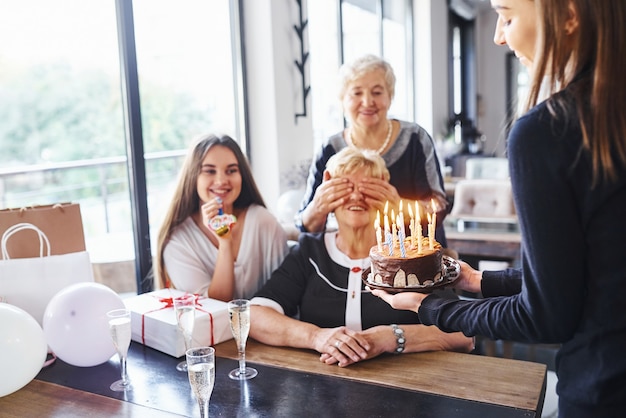 Ältere Frau mit Familie und Freunden, die drinnen Geburtstag feiern.