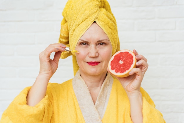 Ältere Frau mit Grapefruit und einer Ölpipette. Konzept der Haut- und Faltenpflege