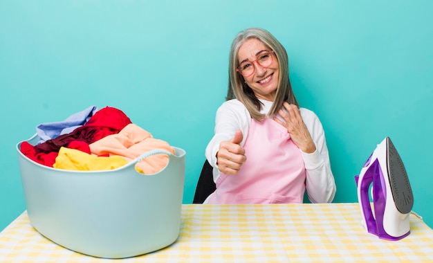 Ältere Frau mit grauen Haaren, die stolz lächelnd positiv mit Daumen nach oben Eisen- und Kleidungskonzept fühlt