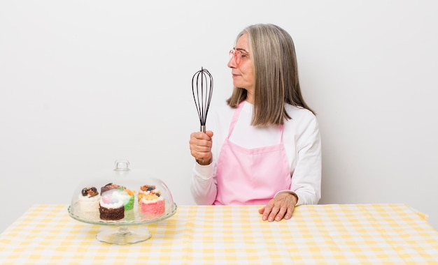 Ältere Frau mit grauen Haaren in der Profilansicht, die sich das Konzept von hausgemachten Kuchen vorstellt oder tagträumt