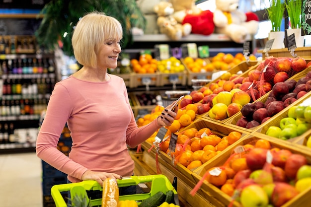 Ältere Frau mit Handy beim Einkaufen im Supermarkt