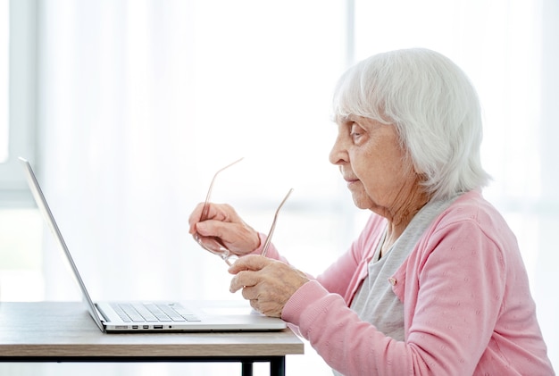 Ältere Frau mit Laptop, die zu Hause sitzt und den Bildschirm betrachtet. Älterer Mensch mit modernen Technologien