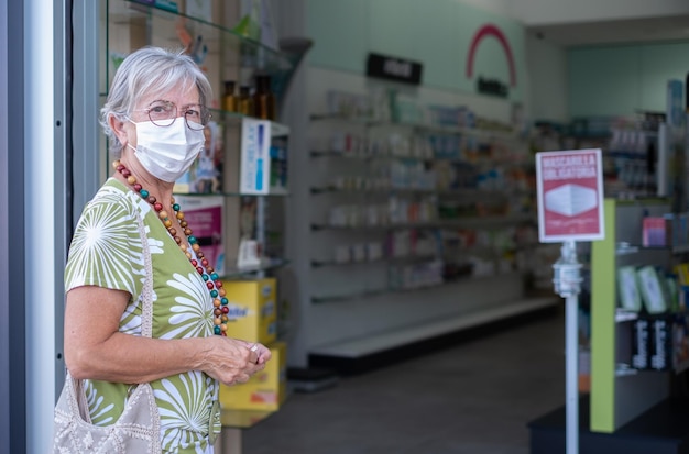 Ältere Frau mit Maske, die in die Apotheke eindringt, um medizinische Produkte zu kaufen Porträt einer gutaussehenden älteren Dame in der Drogerie-Apotheke