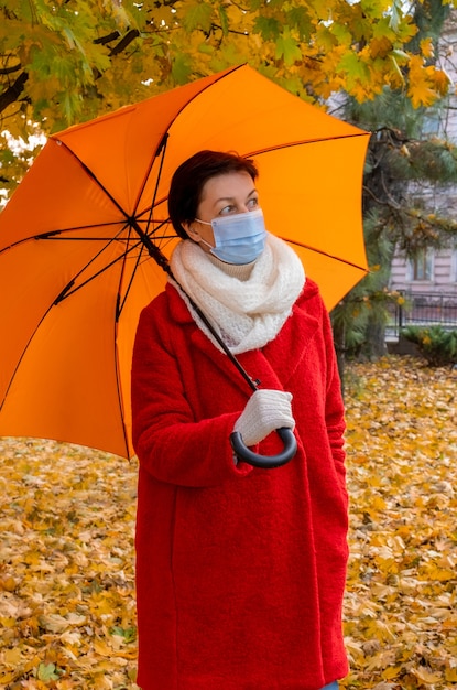 Ältere Frau mit medizinischer Schutzmaske und Regenschirm