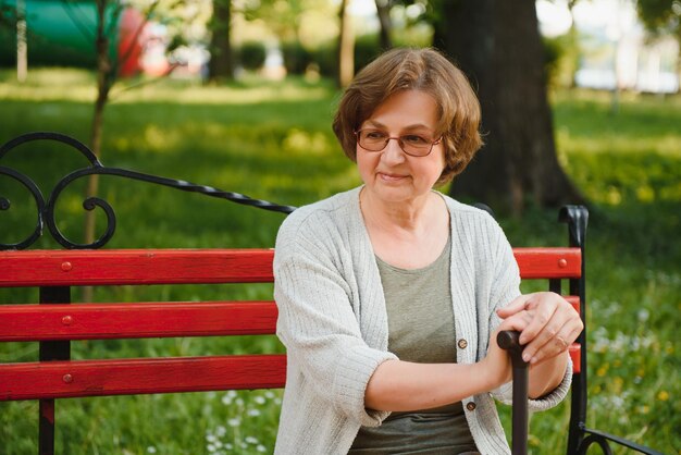 Ältere Frau mit Rohrstock, die auf Bank im Park sitzt