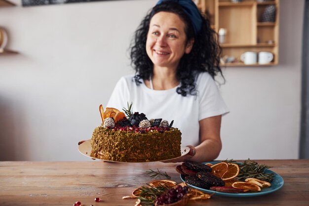 Ältere Frau mit schwarzem lockigem Haar, die diätischen Kuchen in der Küche hält