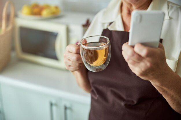 Ältere Frau mit Tasse Tee und Handy