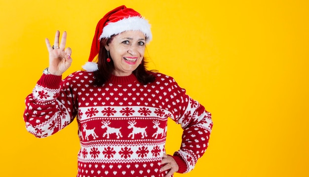 Ältere Frau mit Weihnachtsmütze auf gelbem Hintergrund, lächelnd