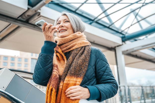 Ältere Frau sendet eine Nachricht mit einem Mobiltelefon in einer Stransport-Station