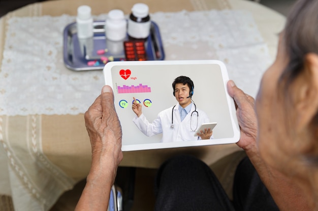 Ältere Frau sitzen zu Hause und haben Online-Beratung mit Arzt auf Tablet-Computer.