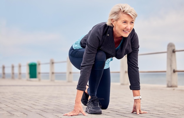 Ältere Frau startet Position und läuft draußen an der Strandpromenade, trainiert oder macht Sky-Attrappe. Ältere Dame ist bereit, für Fitness-Cardio-Training zu laufen und zu lächeln für Sportmarathon, Gesundheit oder Denkweise