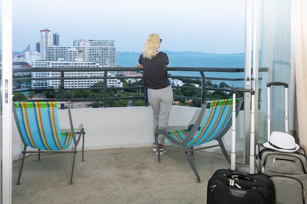 Ältere Frau steht auf dem Balkon und blickt auf die Touristenfrau mit Meerblick im Hotel, nachdem sie ihre Reise und ihren Urlaub eingecheckt hat