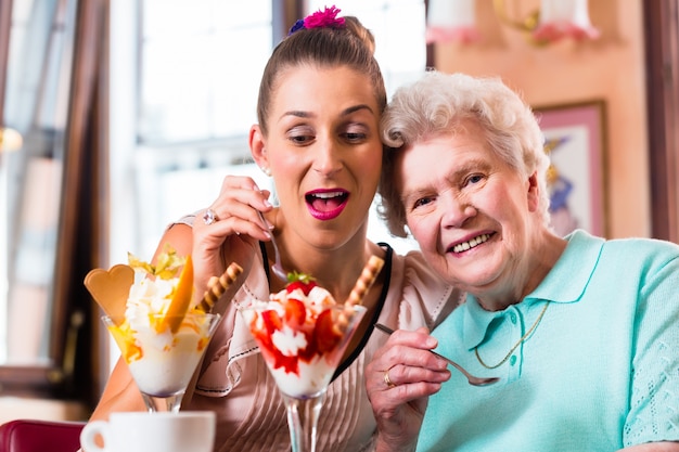 Ältere Frau und Enkelin, die Spaß hat, Eiscremeeiscremebecher im Café zu essen