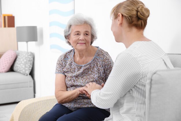 Ältere Frau und Pflegekraft, die zu Hause auf dem Sofa sitzen