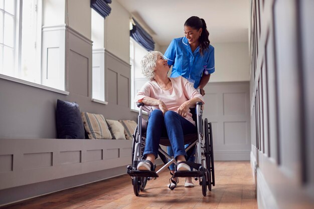 Ältere Frau zu Hause wird von weiblichen Pflegekräften in Uniform in den Rollstuhl geschoben