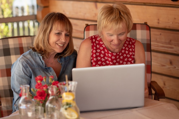 Ältere Frauen lachen beim Blick in den Laptop, während sie zu Hause am Tisch sitzen