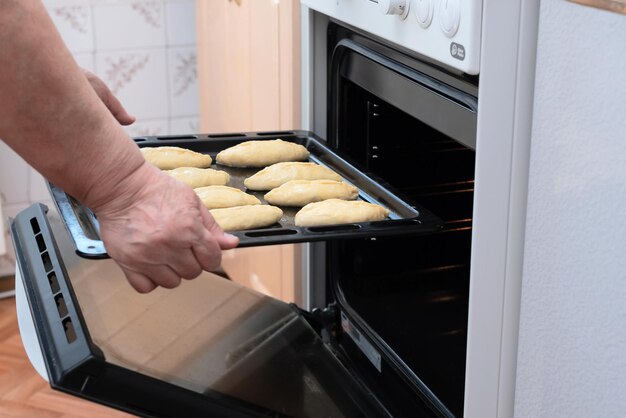 Ältere Frauenhände legen ein Backblech mit rohen Kuchen mit Apfelfüllung in den Ofen Selektiver Fokus Prozess der Herstellung von Kuchen mit Apfelfüllung Kochen zu Hause Konzept Tradition hausgemachtes Essen