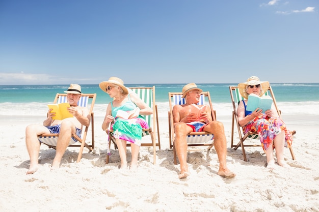 Ältere Freunde, die Bücher auf Strandstühlen lesen