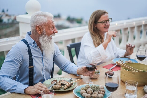 Ältere Freunde, die Spaß bei einer Dinnerparty auf der Terrasse haben - Konzentrieren Sie sich auf das Gesicht des Mannes