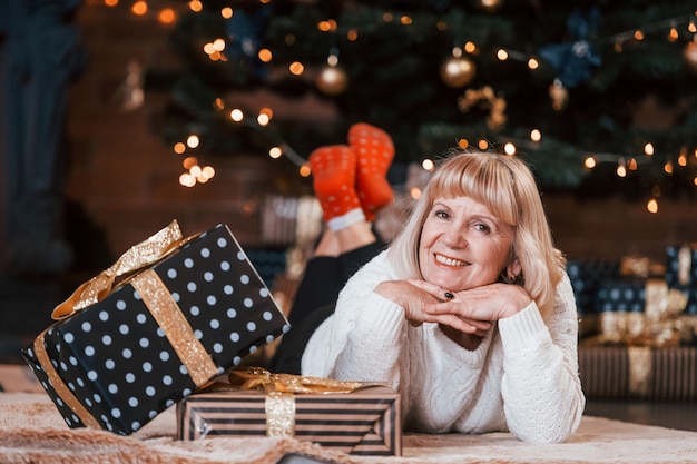 Ältere fröhliche Frau, die sich mit Weihnachtsgeschenkboxen im Raum hinlegt.