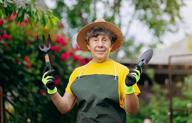 Ältere Gärtnerin mit Hut, die in ihrem Garten mit Arbeitswerkzeugen arbeitet Das Konzept der Gartenarbeit, das Wachsen und Pflegen von Blumen und Pflanzen