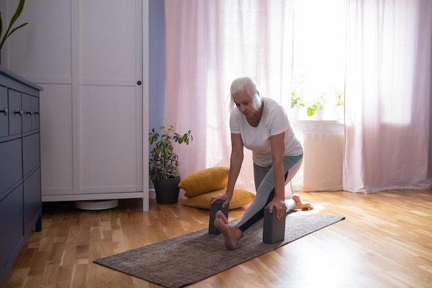 Ältere gealterte Frau, die auf der Yogamatte sitzt und ihre Beine ausdehnt