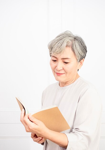 Ältere graue Haare Asiatin, die zu Hause Buch hält und liest.