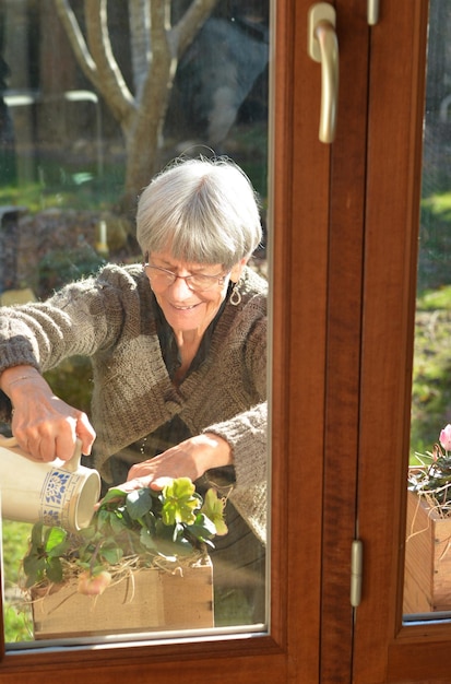 Ältere grauhaarige Dame, die Blumen in einem Garten gießt