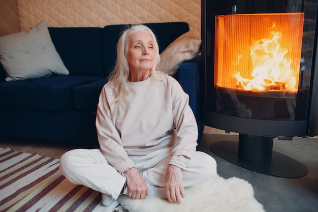 Ältere grauhaarige Frau, die auf Sofa im Wohnzimmer mit Kamin sitzt.