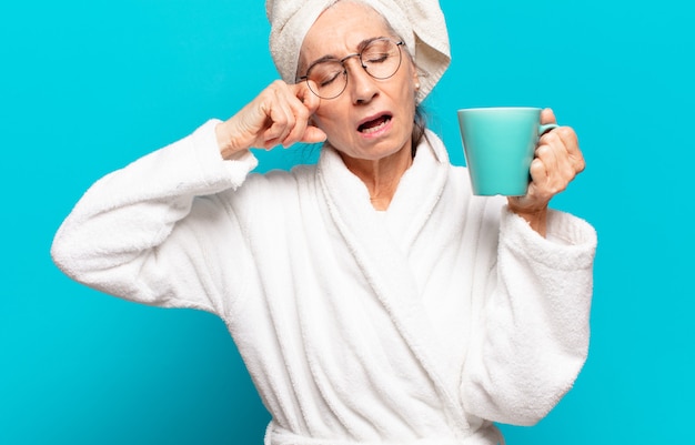 Ältere hübsche Frau, die Bademantel trägt und einen Kaffee trinkt