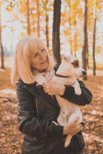 Ältere lächelnde Frau, die ihren Hund im Herbstpark umarmt. Aktives Altern und Haustierkonzept.