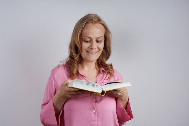 Ältere Lehrerin im rosa Hemd, die ein Buch liest. Bildungskonzept.