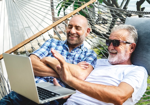 Ältere Männer, die auf einer Hängematte unter Verwendung eines Laptops liegen