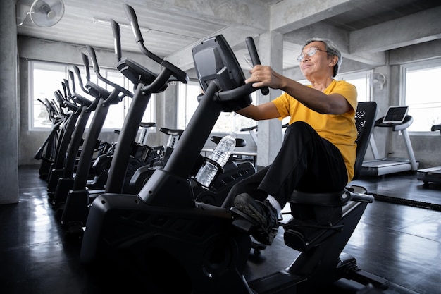 Ältere Männer trainieren, indem sie das Fahrrad im Fitnessstudio drehen. Konzept von gesunden älteren Menschen mit Übung. Asiatische reife Männer, die Trainingsgeräte im Fitnessstudio spielen
