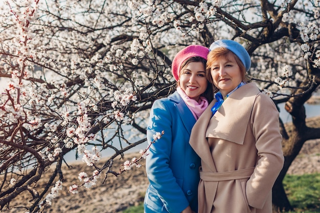 Ältere Mutter und ihre erwachsene Tochter, die im Frühling blühenden Park umarmen