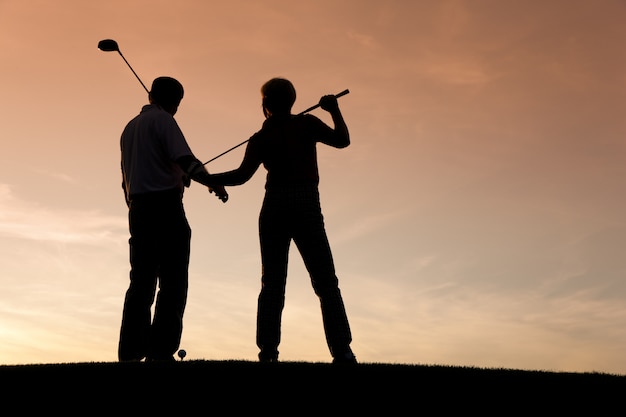 Ältere Paare, die Golf bei Sonnenuntergang spielen