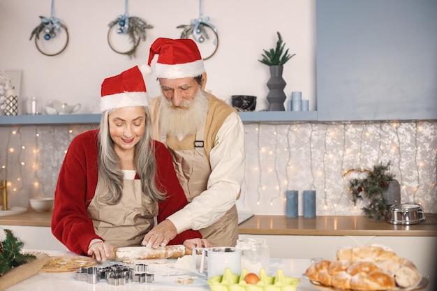 Ältere Paare in den roten Weihnachtshüten, die in der Küche kochen