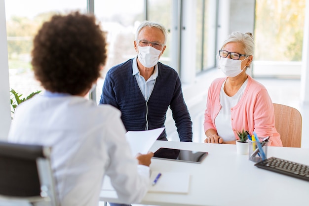 Ältere Paare mit schützenden Gesichtsmasken erhalten Nachrichten von einer schwarzen Ärztin im Büro