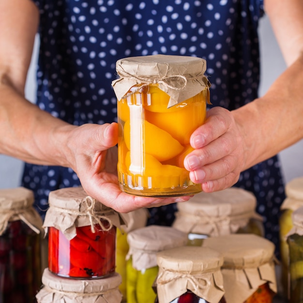 Ältere reife Frau, die in den Händen Glas mit hausgemachtem konserviertem und fermentiertem Essen hält. Vielzahl von eingelegtem und mariniertem Gemüse, Obstkompott. Hauswirtschaft, Hauswirtschaft, Ernteerhaltung