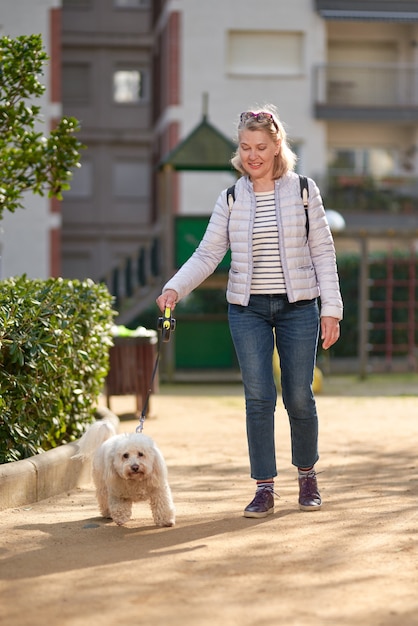 Ältere Rentnerfrau gehen Park weißen kleinen Hund.