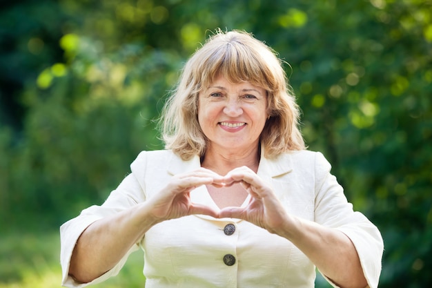 Ältere schöne Frau lächelnd, die ein Herz mit den Händen macht