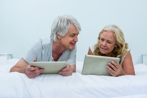 Ältere sprechende Paare bei der Anwendung von digitalen Tabletten im Schlafzimmer