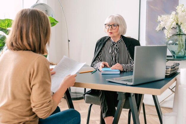 Ältere stilvolle Frau mit junger Frau, die Arbeitsaufgaben im Büro bespricht