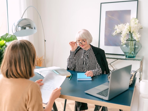 Ältere stilvolle Frau mit junger Frau, die Arbeitsaufgaben im Büro bespricht