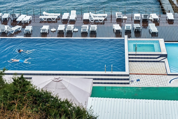 Ältere Touristenpaare schwimmen im Hotelpool gegen leere Strandliegen und Meer