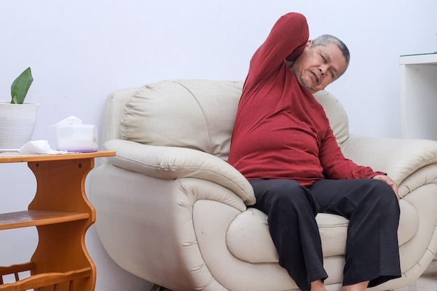 Älterer älterer Mann fühlt Schmerzen im Rücken und Nacken, während er zu Hause auf dem Sofa sitzt