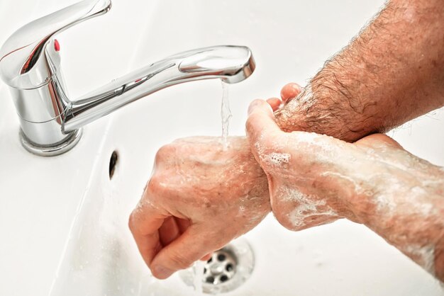 Älterer älterer Mann seine Hände und sein Handgelenk unter Leitungswasserhahn, Detailfoto. Kann als Hygiene-Illustrationskonzept während der Prävention von Coronavirus/Covid-19-Ausbrüchen verwendet werden